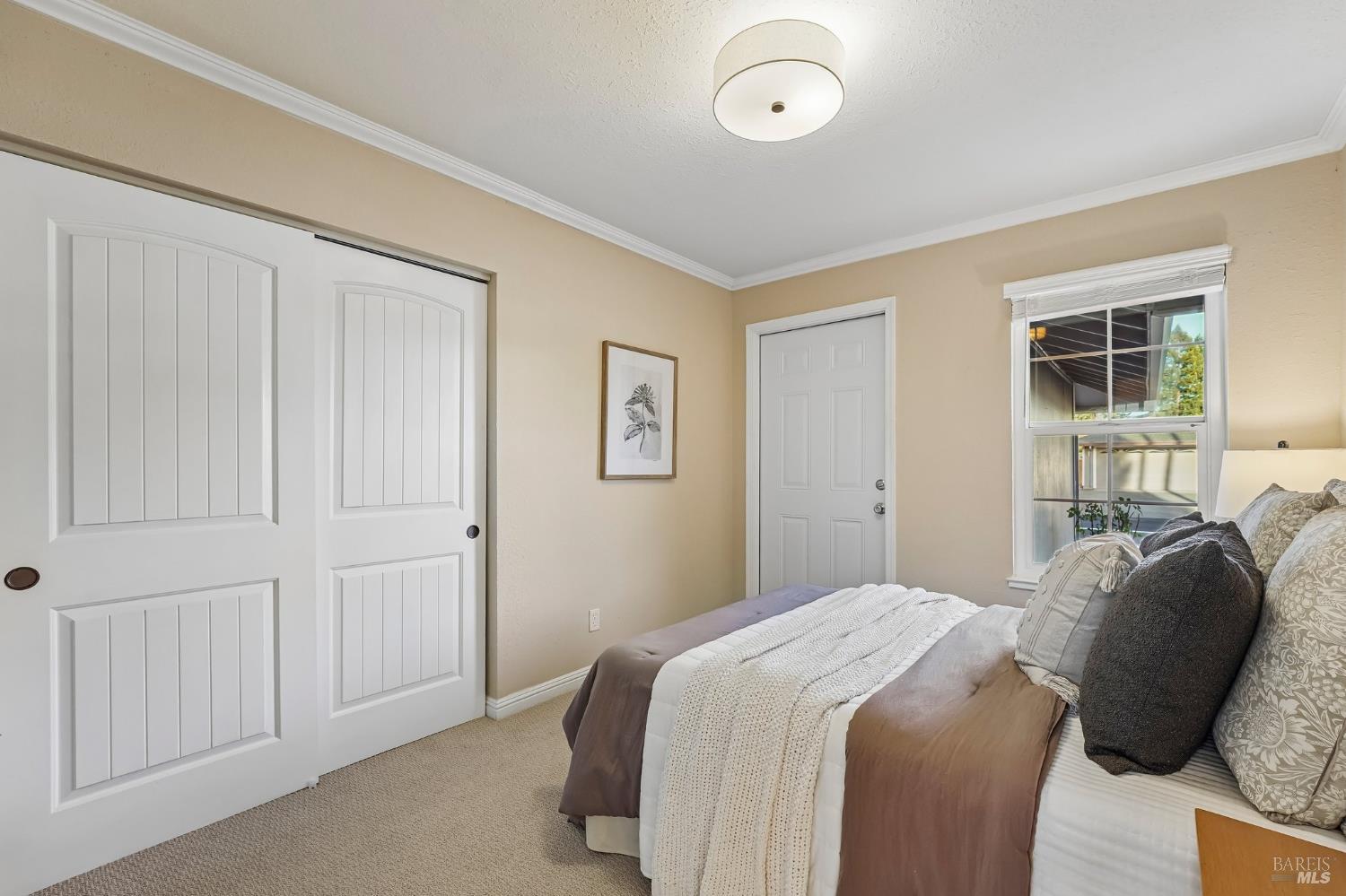 Staged bedroom with white sliding closet doors and a bed beside a window.