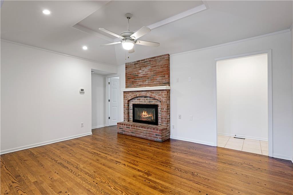 Empty living room with hardwood floors and a brick fireplace beneath a ceiling fan.