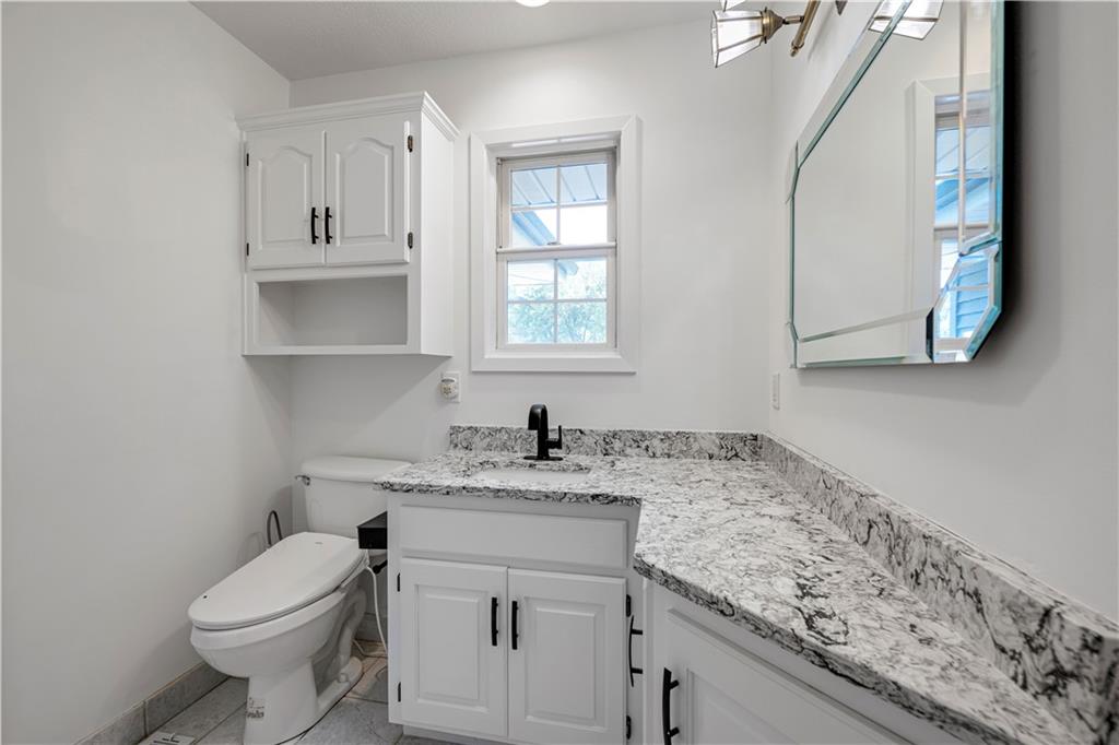Bathroom with a white vanity, marbled countertop, black faucet, and toilet beneath a window.