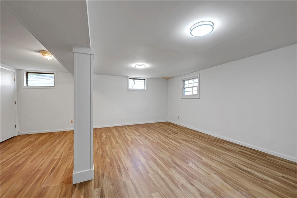 Finished basement room with wood-look flooring, small windows, and a central support column.