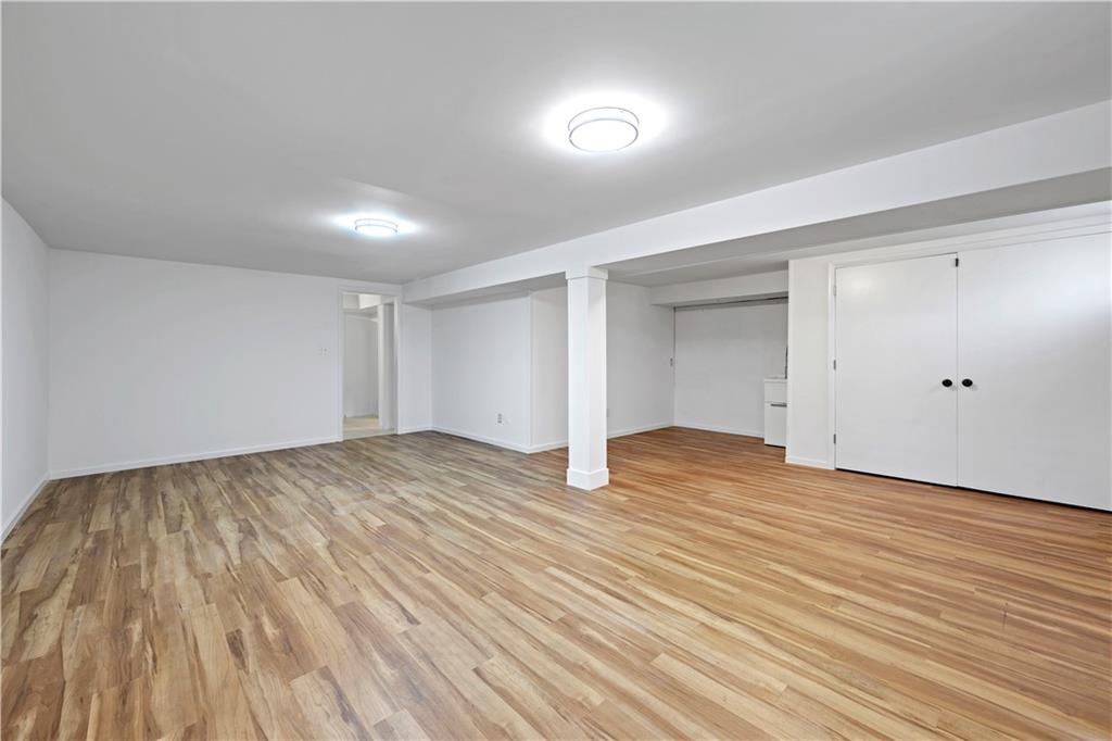 Empty finished basement with wood-look flooring, a support column, and double-door closet.