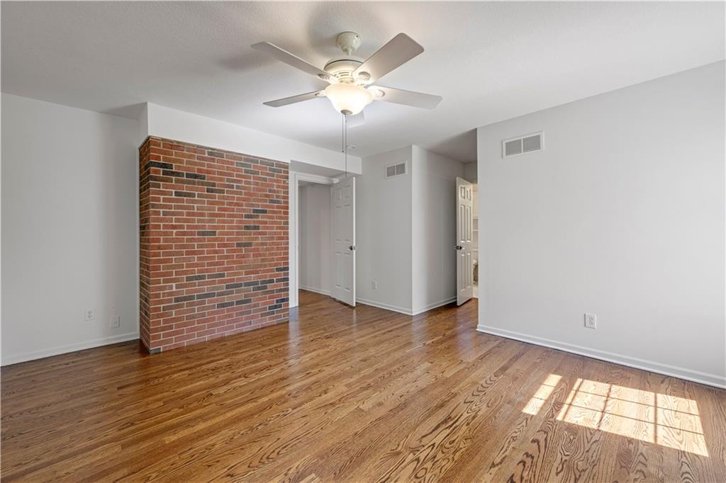 Empty living room with hardwood floors, a red brick accent wall, and a ceiling fan.