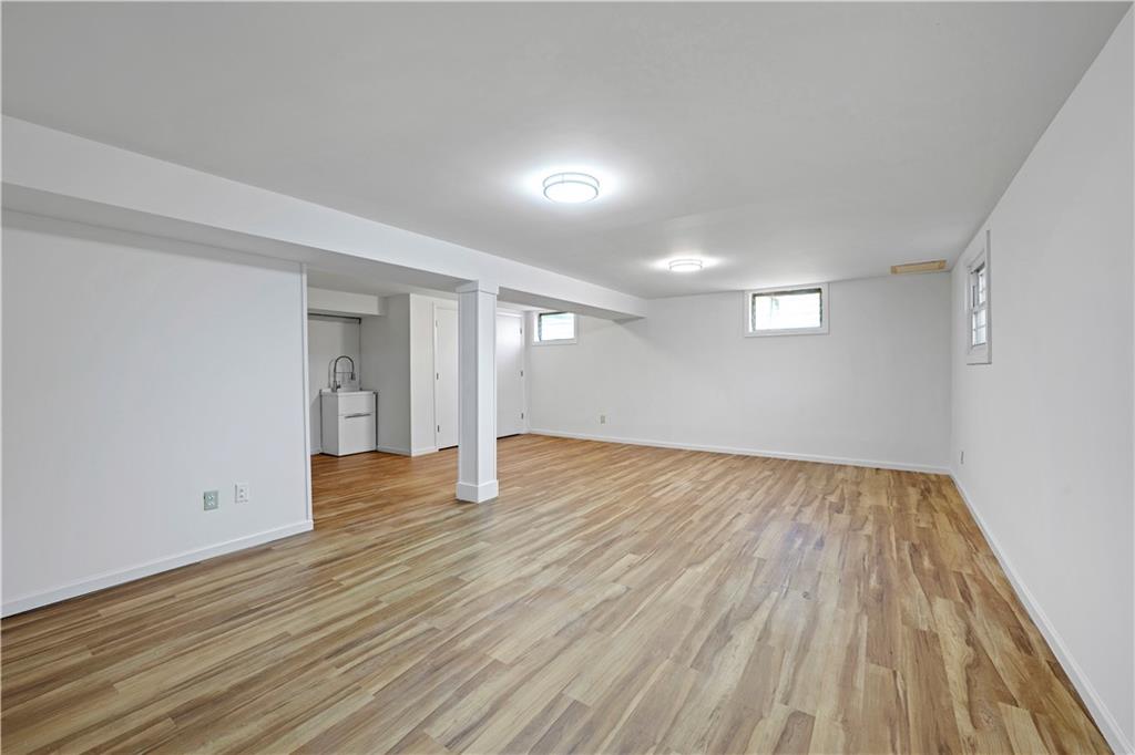 Empty basement with wood-look plank flooring, small windows, and a utility sink.