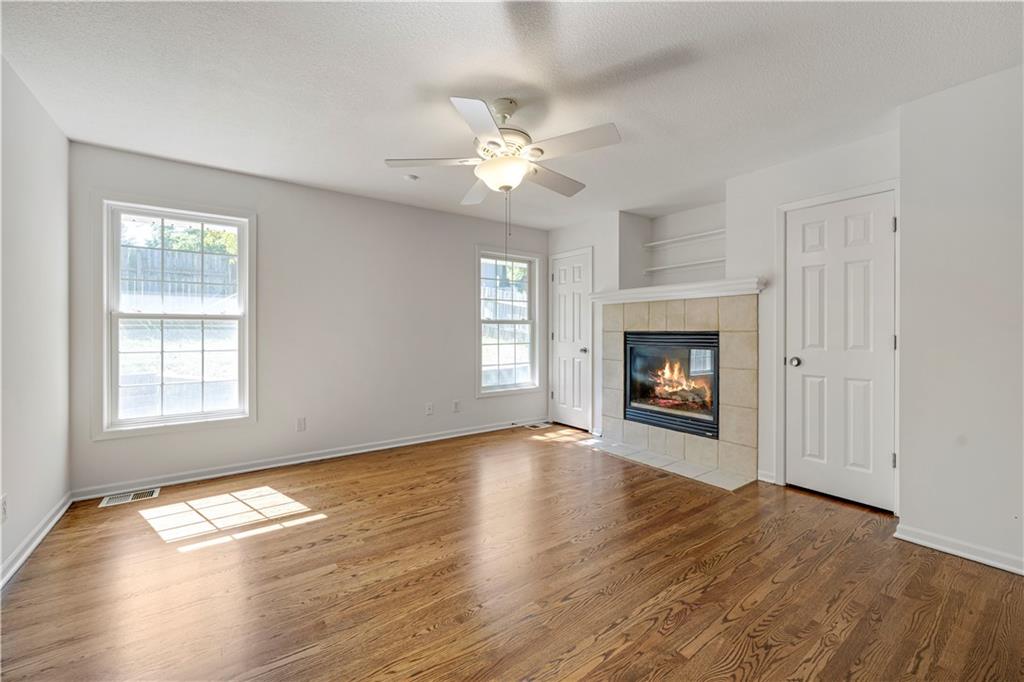Living room with hardwood floors, a tiled fireplace, and sunlight streaming through two windows.