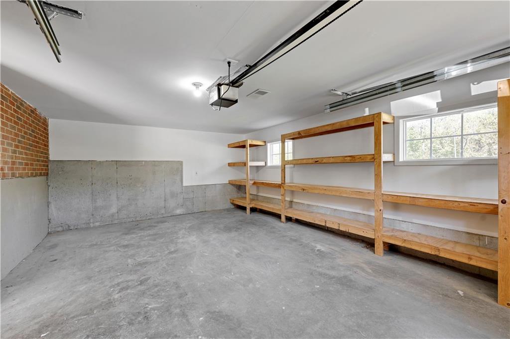Empty garage with a concrete floor, long wooden storage shelves, and two windows.
