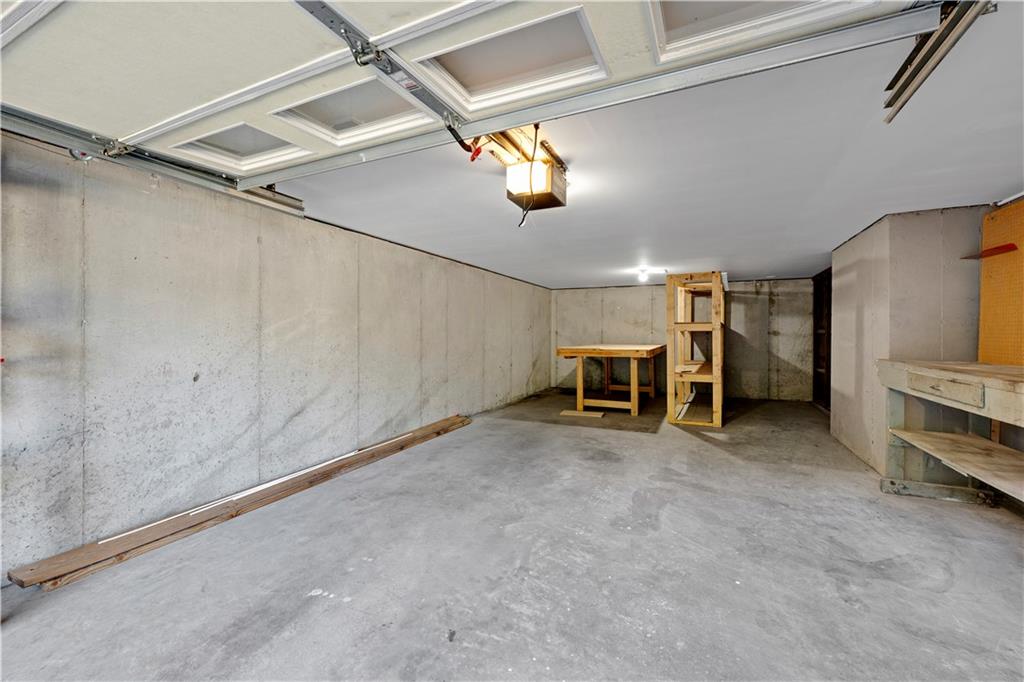 Empty concrete garage with an open overhead door, workbenches, and storage shelving.