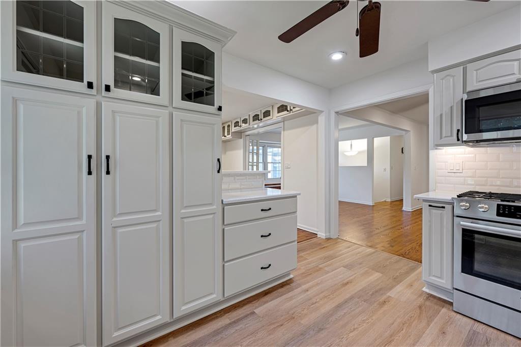 Kitchen with tall white cabinets, glass-front uppers, stainless steel appliances, and wood flooring.