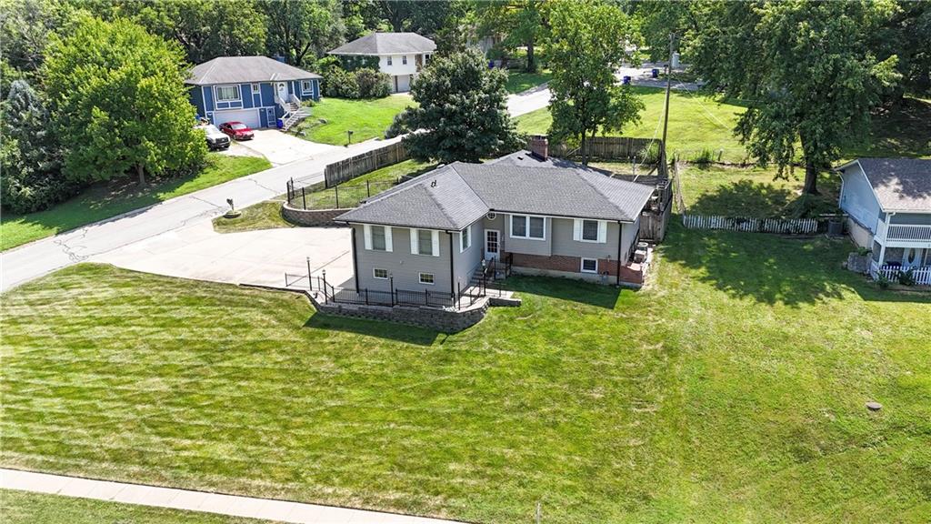 Aerial view of a gray home with a fenced patio and broad green lawn.