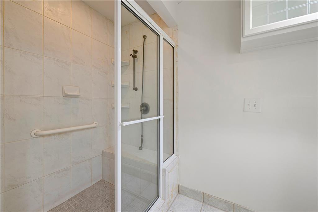 Tiled walk-in shower with a glass enclosure, grab bar, and high window.
