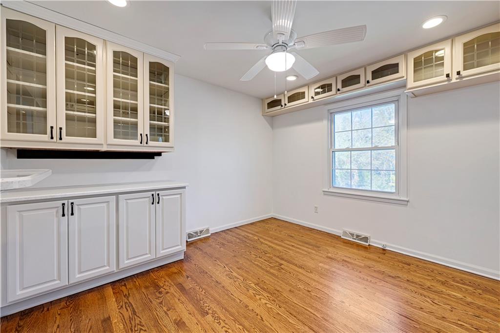 Empty room with built-in white glass-front cabinets, hardwood floors, and a ceiling fan.