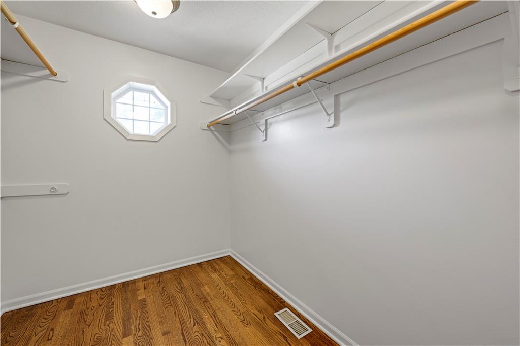 Empty walk-in closet with built-in hanging rods, shelves, and an octagonal window.