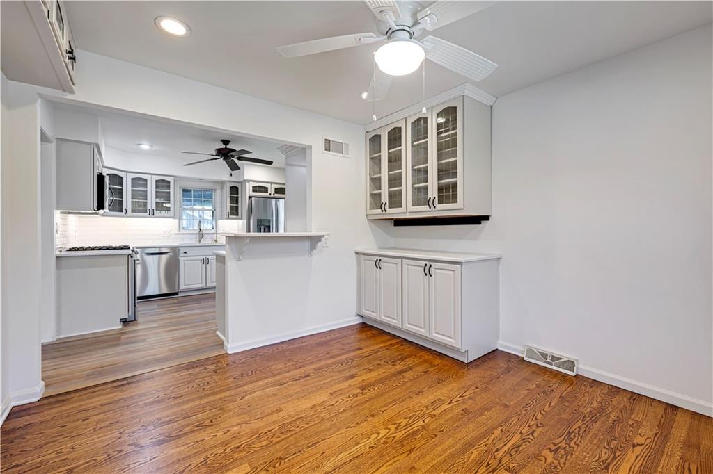 Dining area with hardwood floors and built-in cabinets, opening to a white kitchen with stainless steel appliances.
