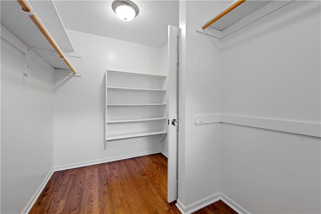 Walk-in closet with built-in shelves, wooden hanging rods, and hardwood floors.