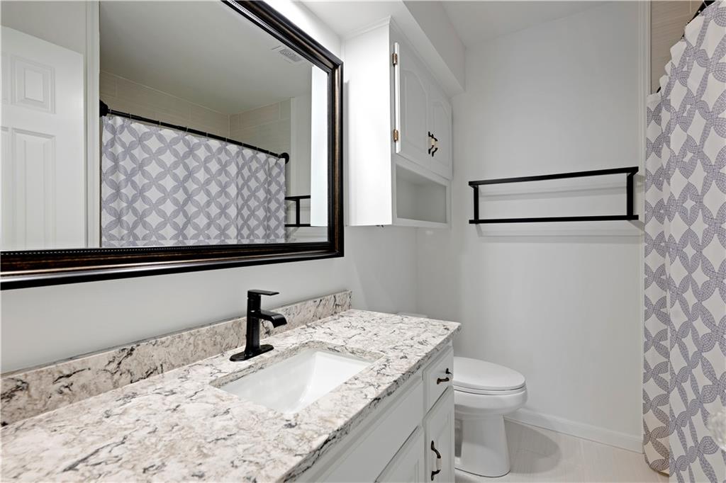 Bathroom with a marbled vanity, black faucet, large mirror, and gray patterned shower curtain.
