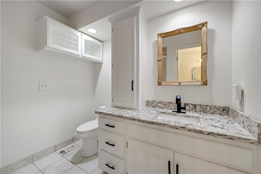 Bathroom with a white vanity, stone countertop, framed mirror, and overhead cabinets.