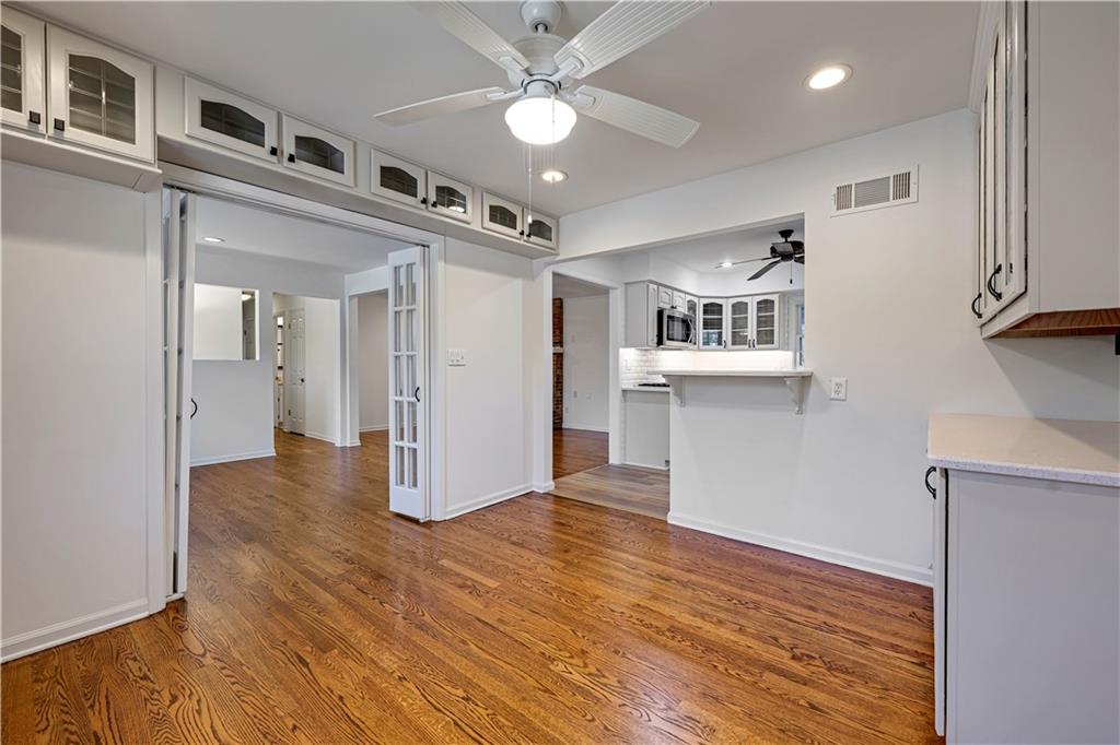 Empty dining area with warm wood floors, white built-in cabinetry, and French doors beside the kitchen.