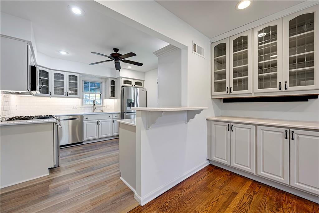 Kitchen with white cabinets, stainless steel appliances, glass-front cupboards, and a raised breakfast bar.