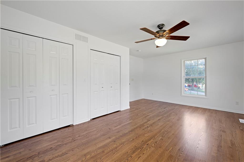 Empty bedroom with two sets of closets, hardwood floors, and a ceiling fan.