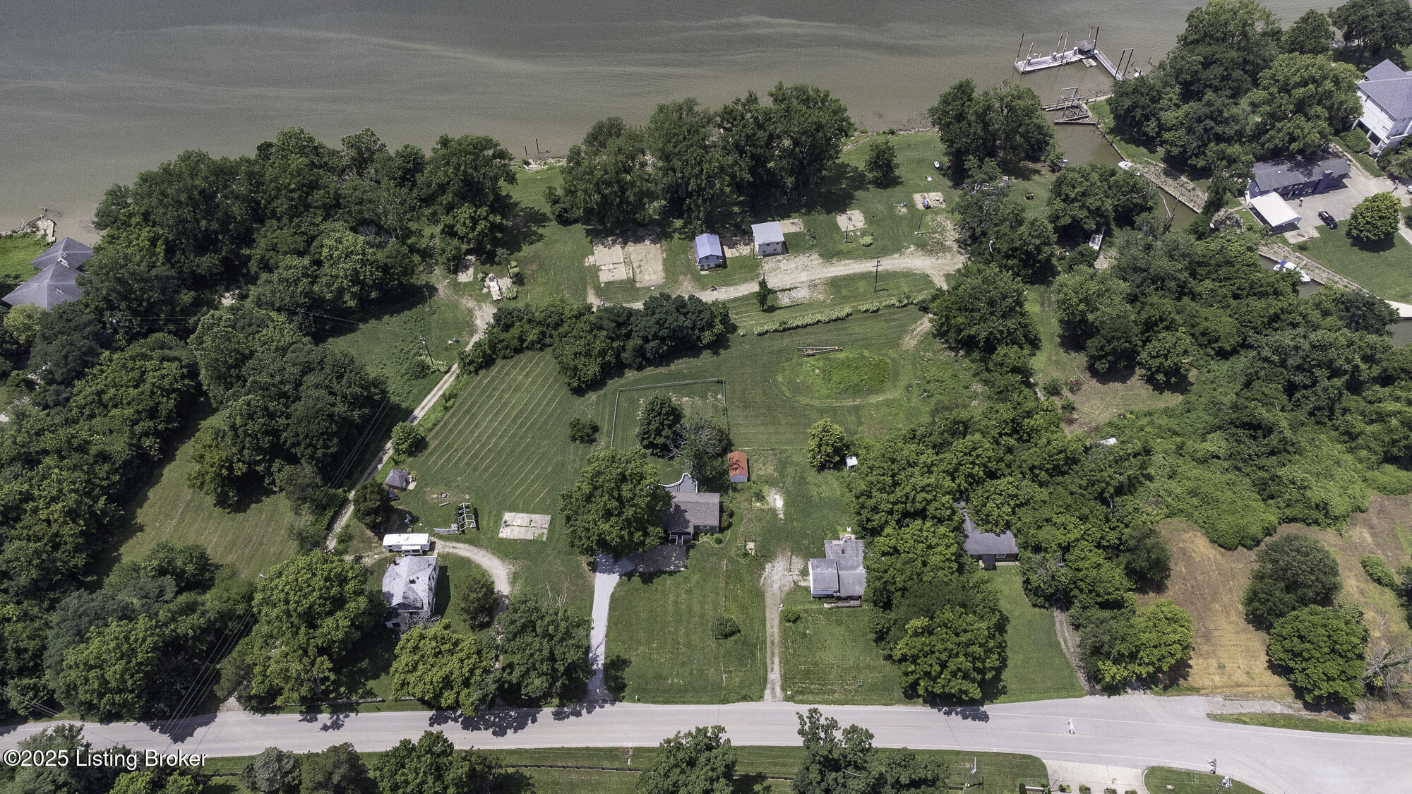 Aerial view of wooded riverfront lots with homes, lawns, and docks along the water.