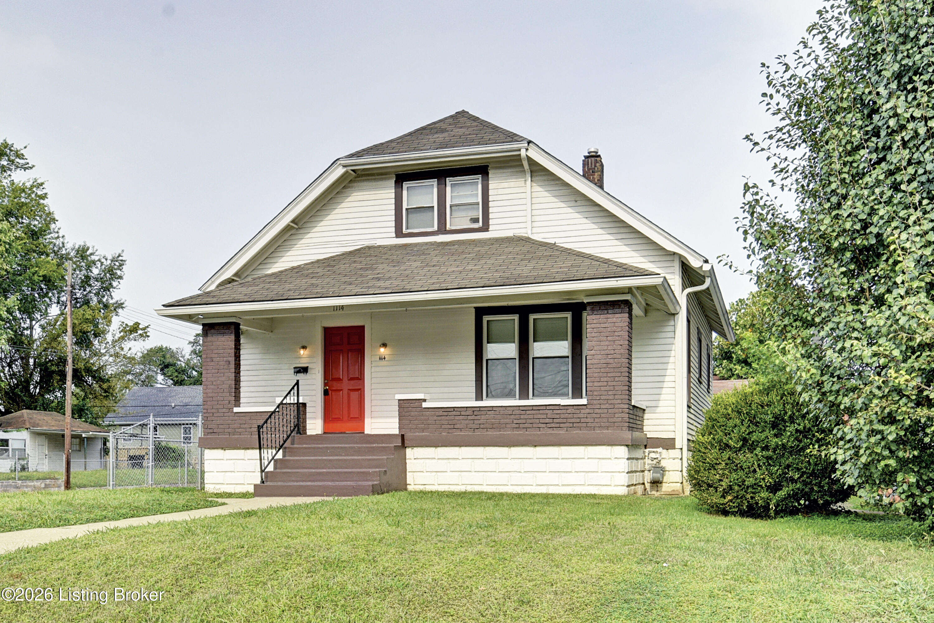 White gable-front house with a red front door, brick porch columns, and a green lawn.