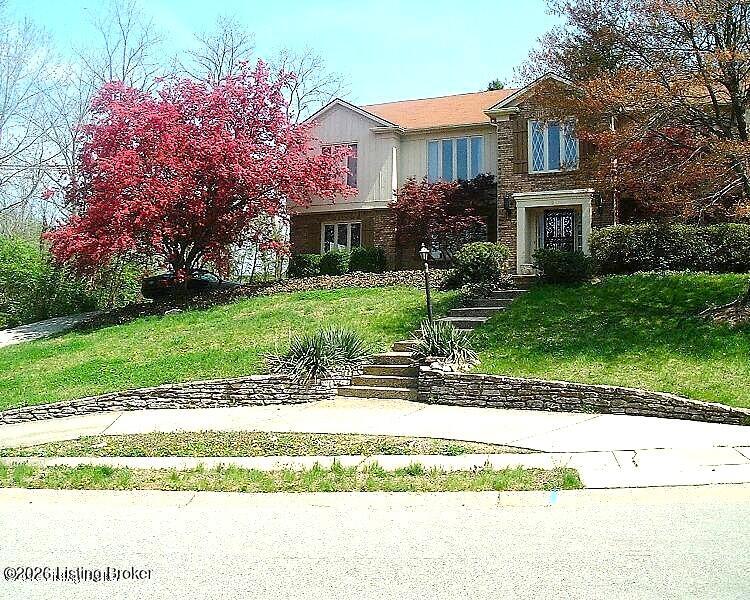 Two-story house above a sloped lawn, with stone steps and a pink-flowering tree.