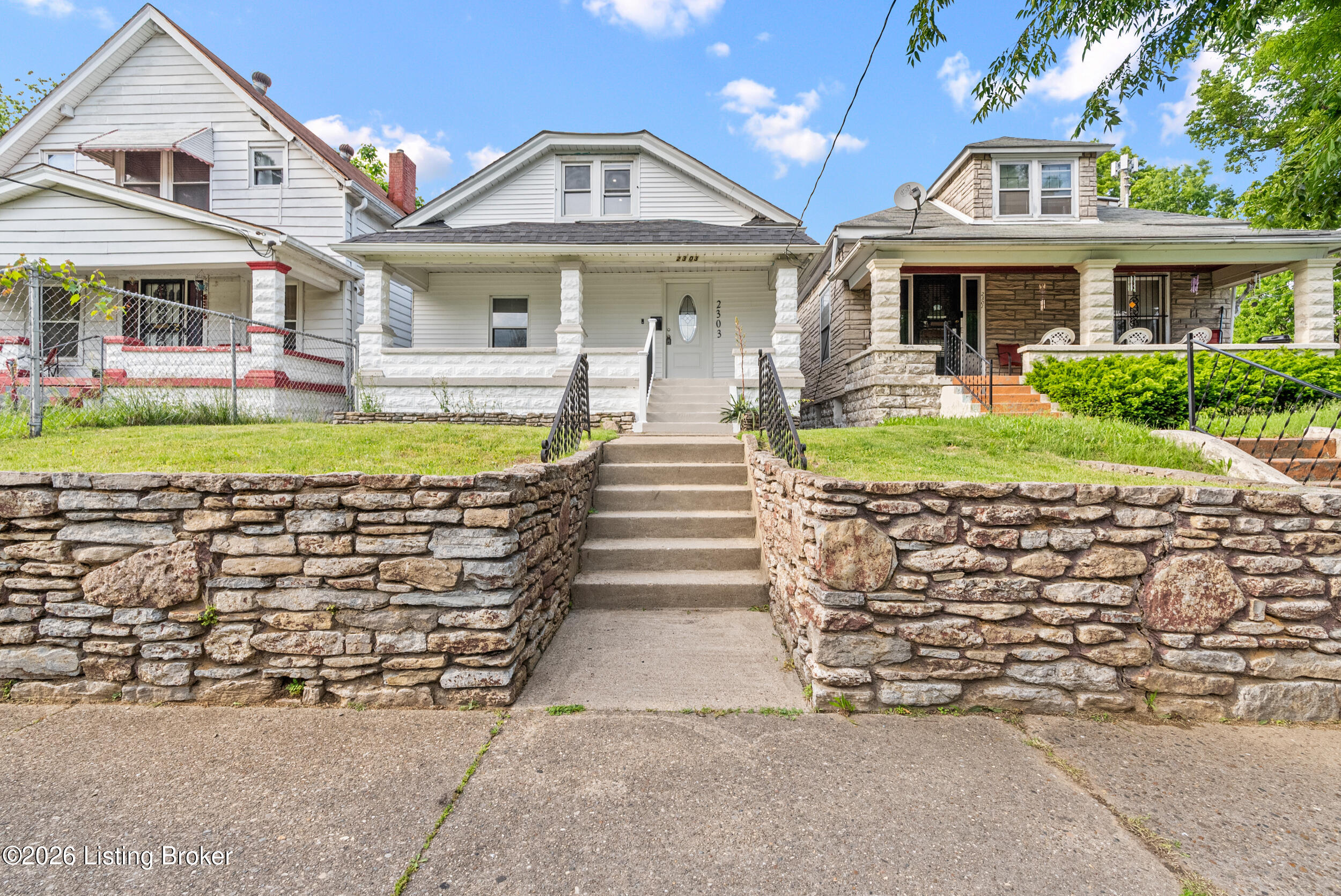 White-sided house with a covered porch, stone retaining walls, and concrete front steps.