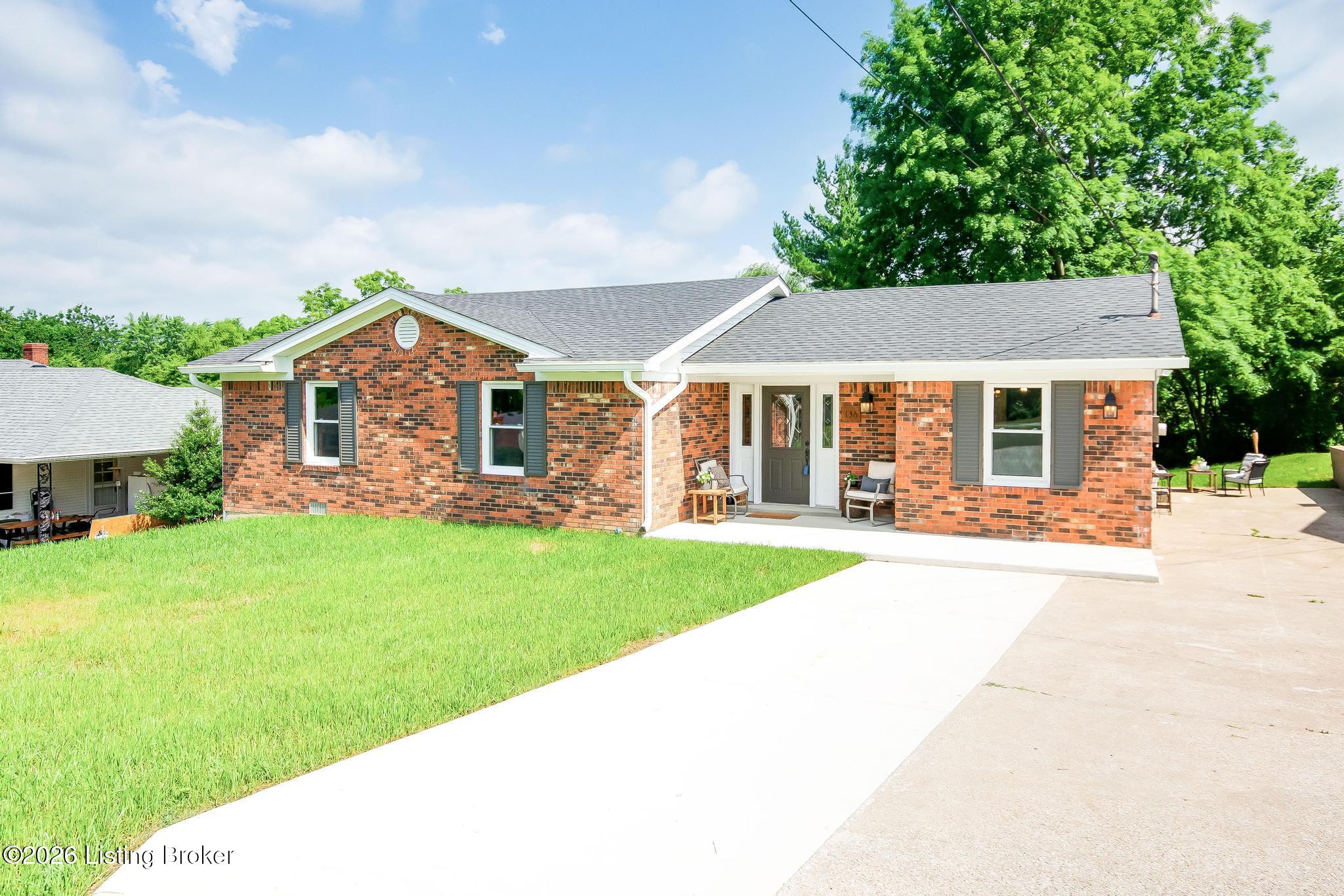 Red brick ranch home with gray shutters, a covered front entry, and a wide concrete driveway.