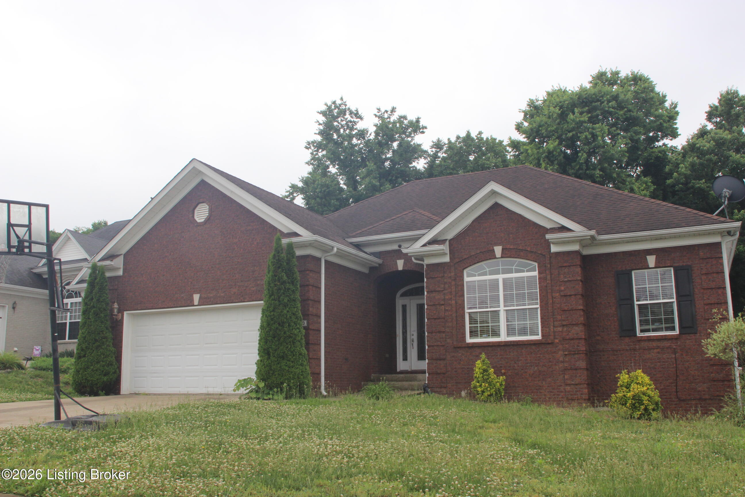 Red-brick house with white garage, arched entry, broad lawn, and a basketball hoop by the driveway.