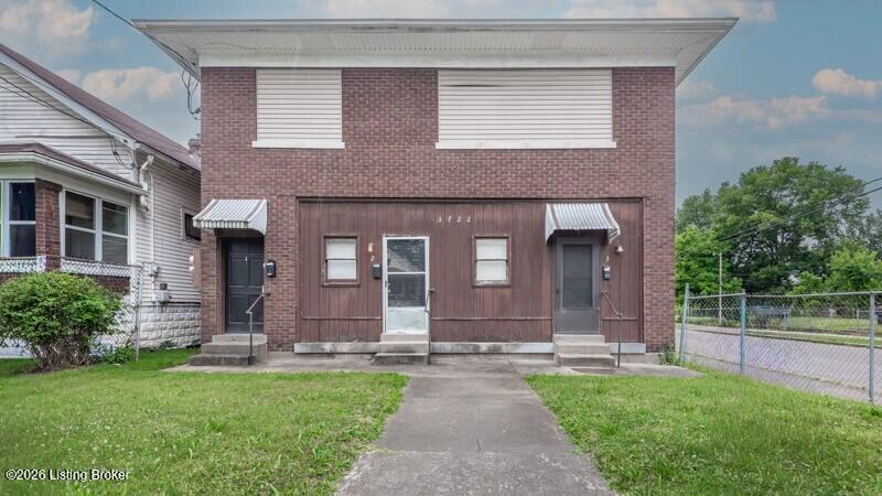 Two-story brick building with two entrances, metal awnings, and a walkway across the lawn.