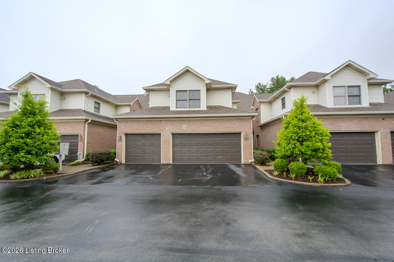 Two-story attached home with brick facade, two garage doors, and landscaped shrubs.