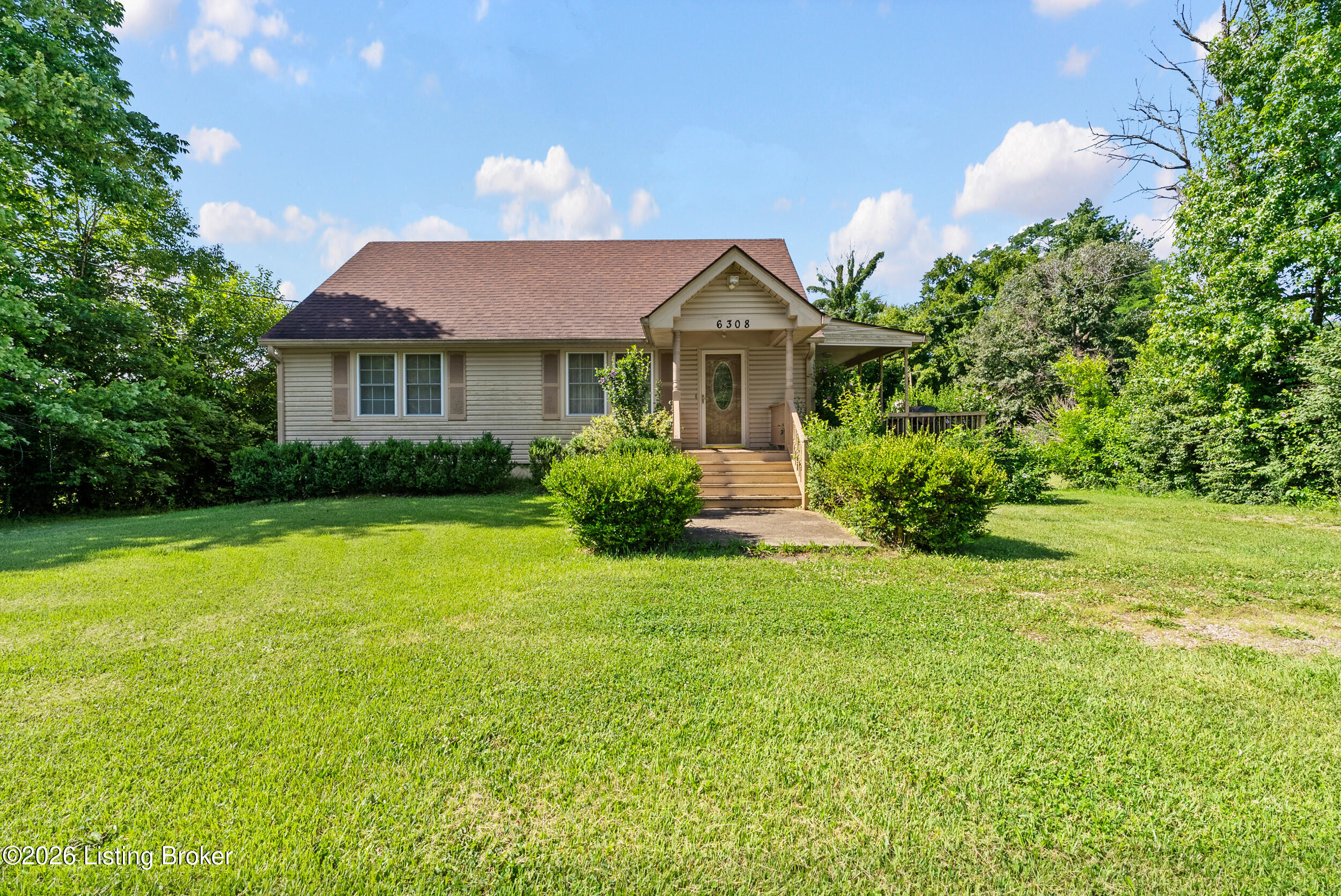 Beige single-story house with a covered entrance, front steps, and a broad green lawn.