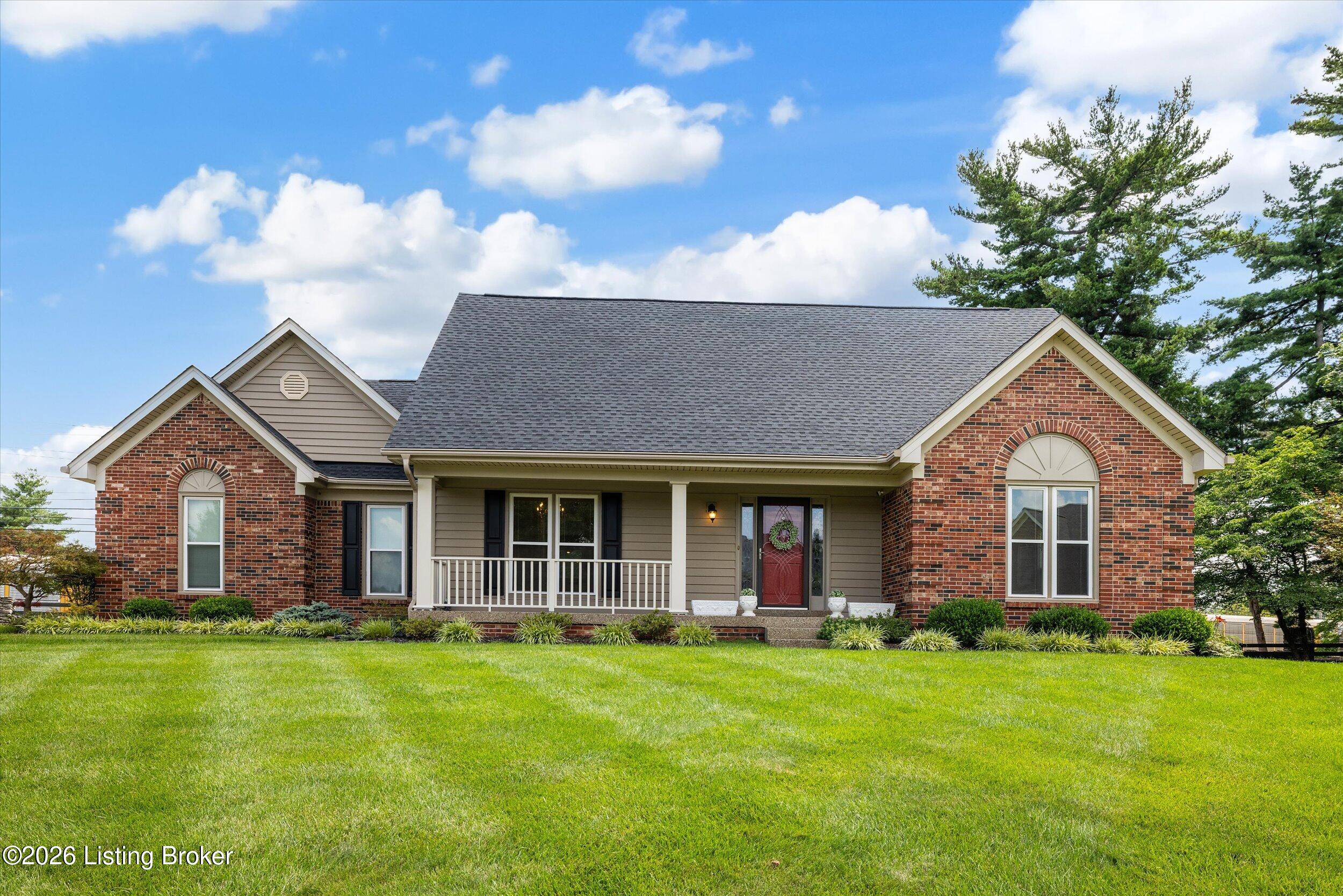 Single-story brick and gray-sided home with a broad covered porch, arched windows, and a green front lawn.