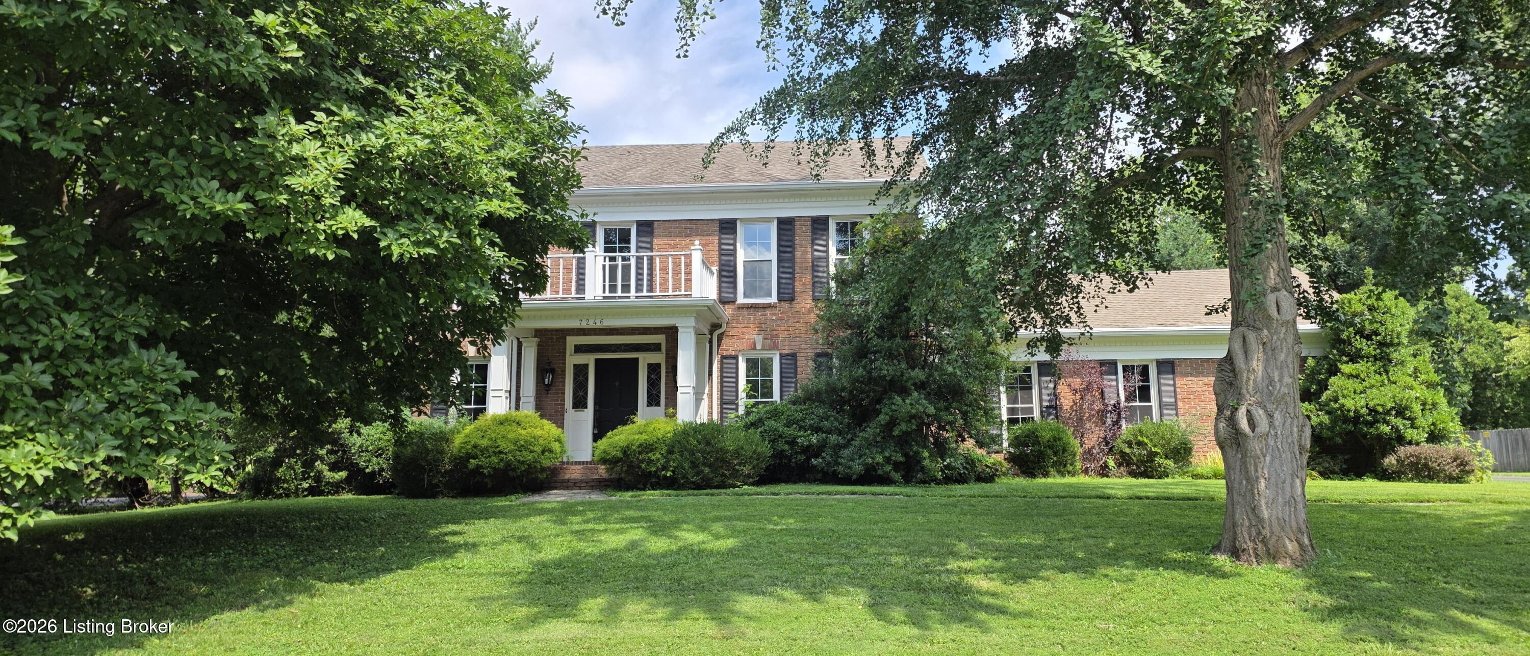 Two-story brick house with a white-columned entrance, framed by mature trees and a broad lawn.