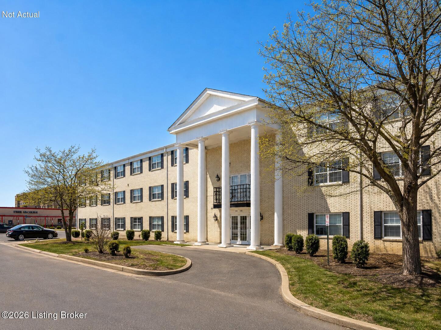 Beige-brick building with a columned entrance, black shutters, and a curved driveway.