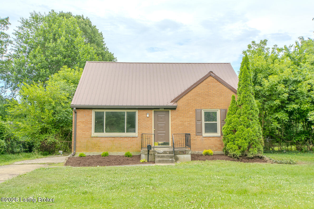 Brick house with a light metal roof, front steps, and a lawn surrounded by mature trees.