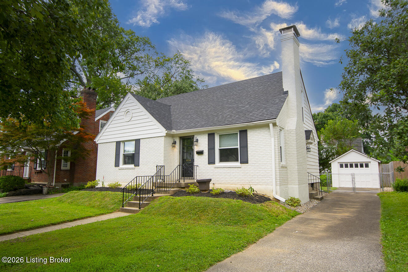 White brick Cape Cod-style house with a tall chimney, detached garage, and long driveway.