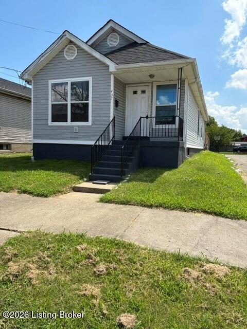 Gray-sided house with white trim, a covered porch, black railings, and steps facing a concrete walkway.