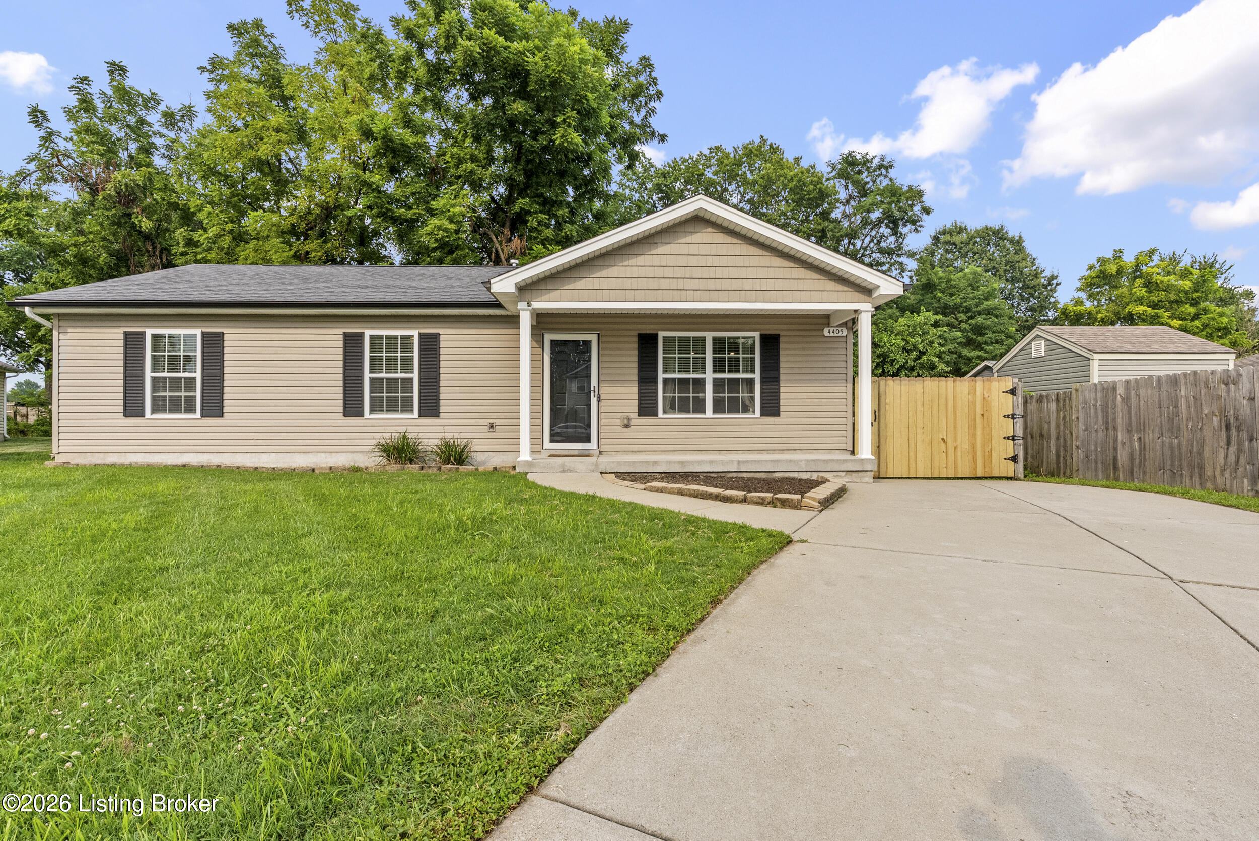 Single-story beige house with a covered entry, front lawn, and wide concrete driveway.