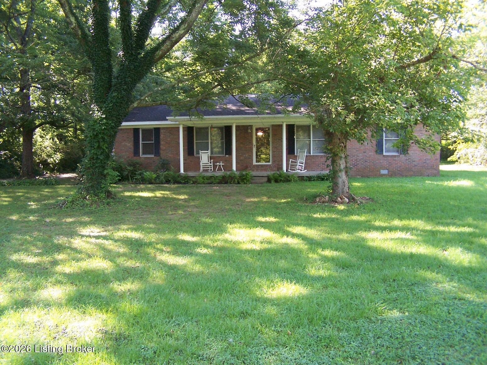 Single-story brick home with a covered porch, rocking chairs, and a broad shaded lawn.