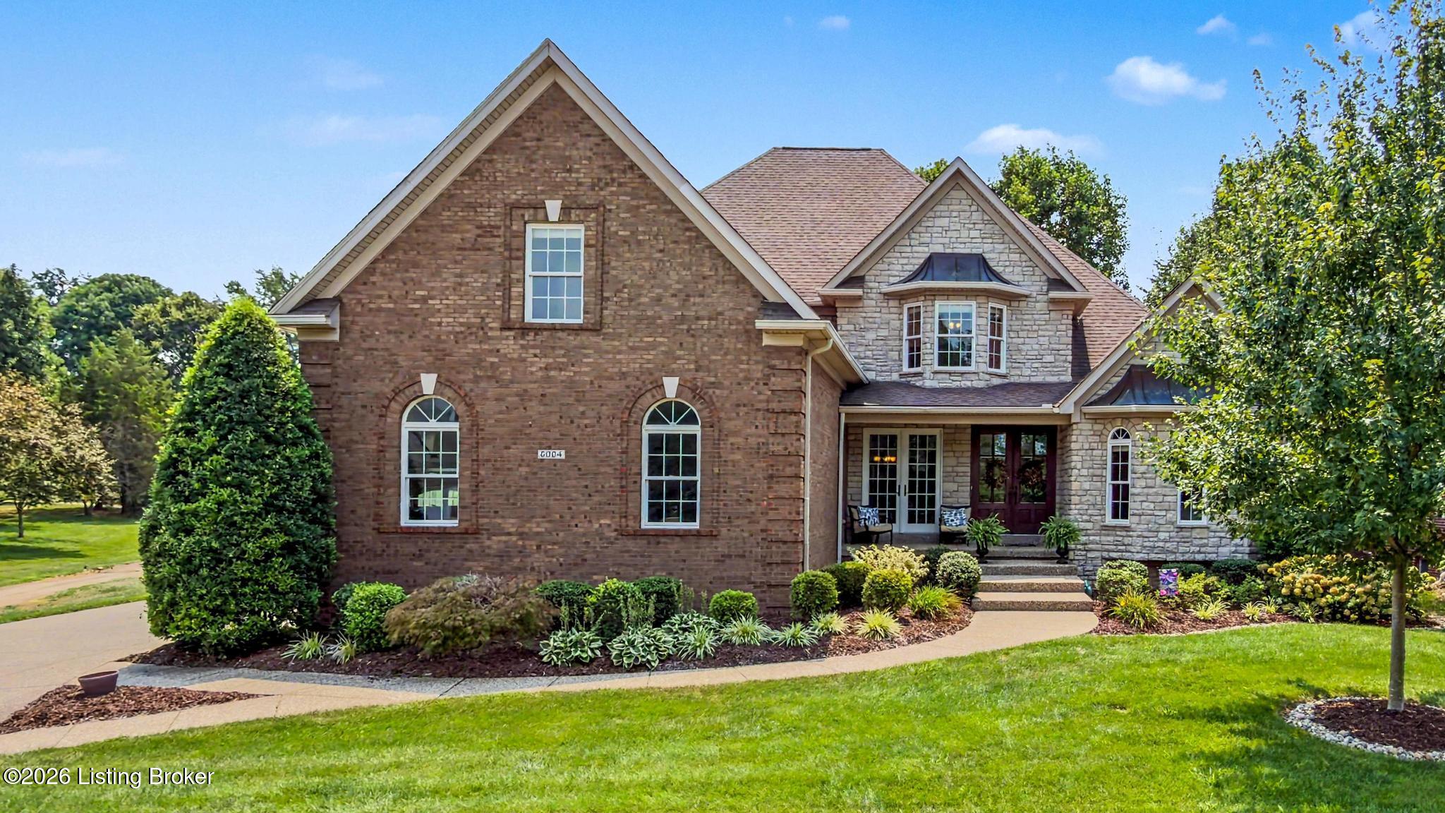 Two-story brick and stone home with arched windows, landscaped gardens, and a curved front walkway.