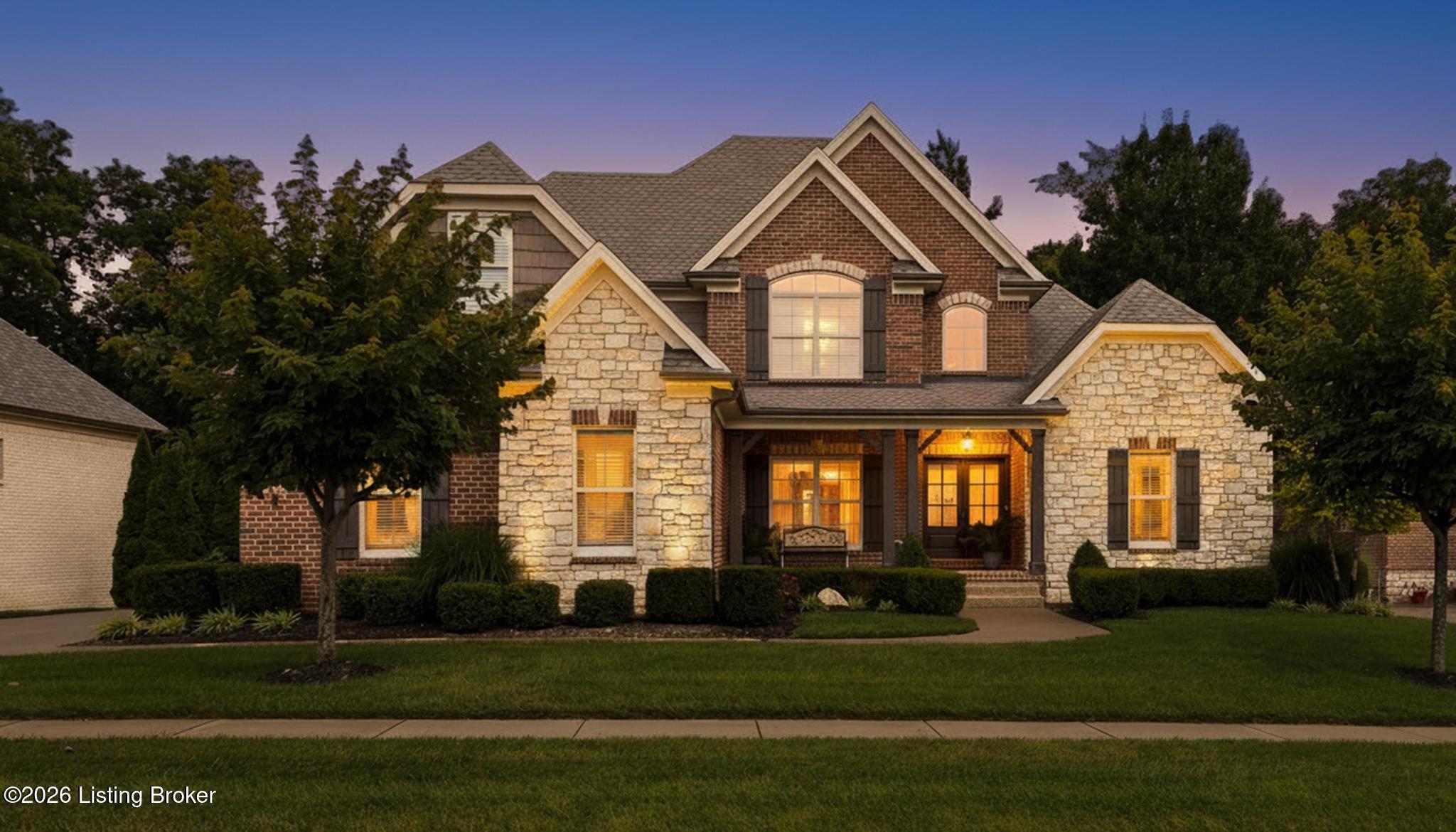 Two-story brick and stone house at dusk with glowing windows and a covered front entry.