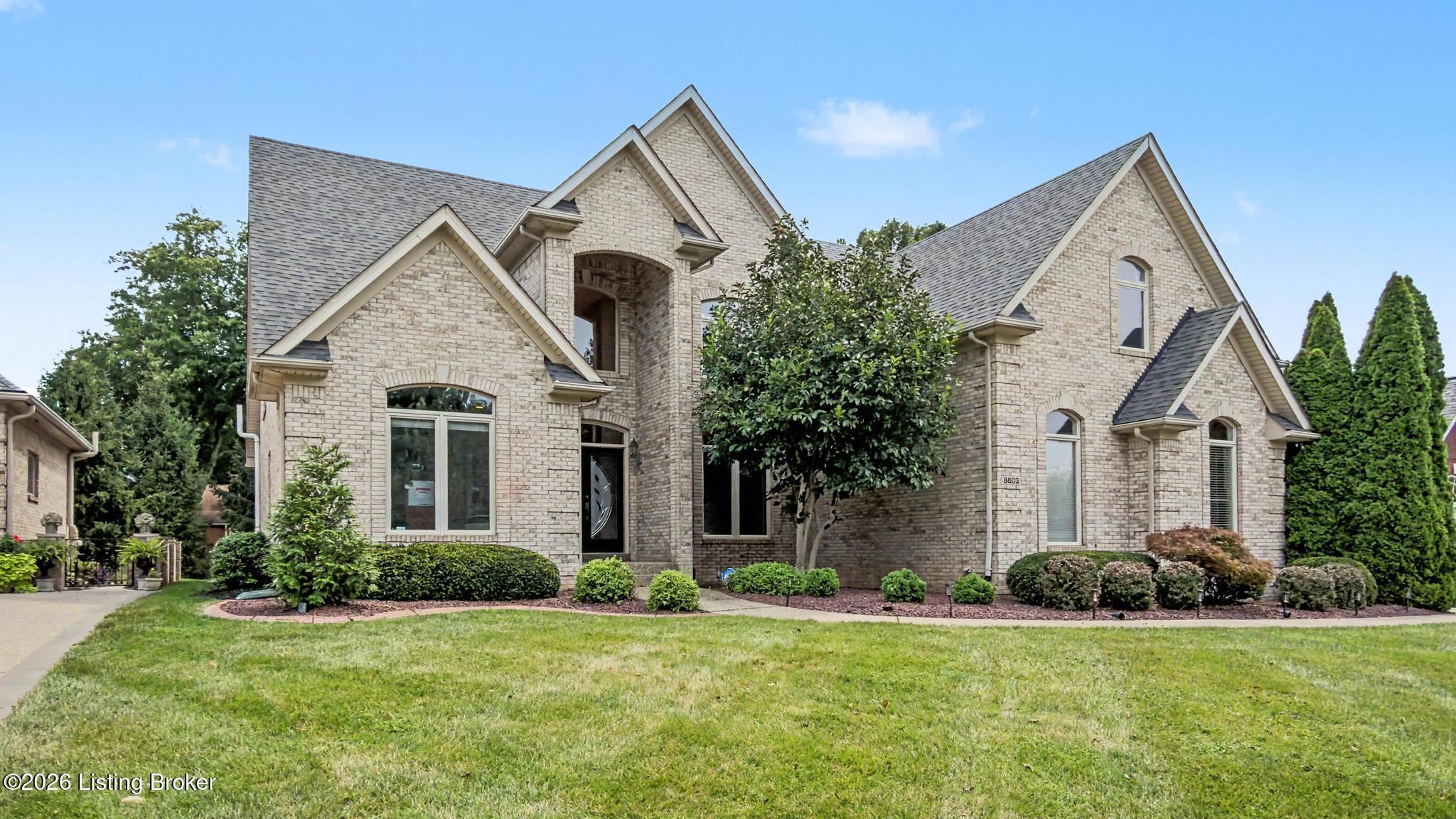 Large light-brick home with multiple gables, arched entry, and landscaped front lawn.