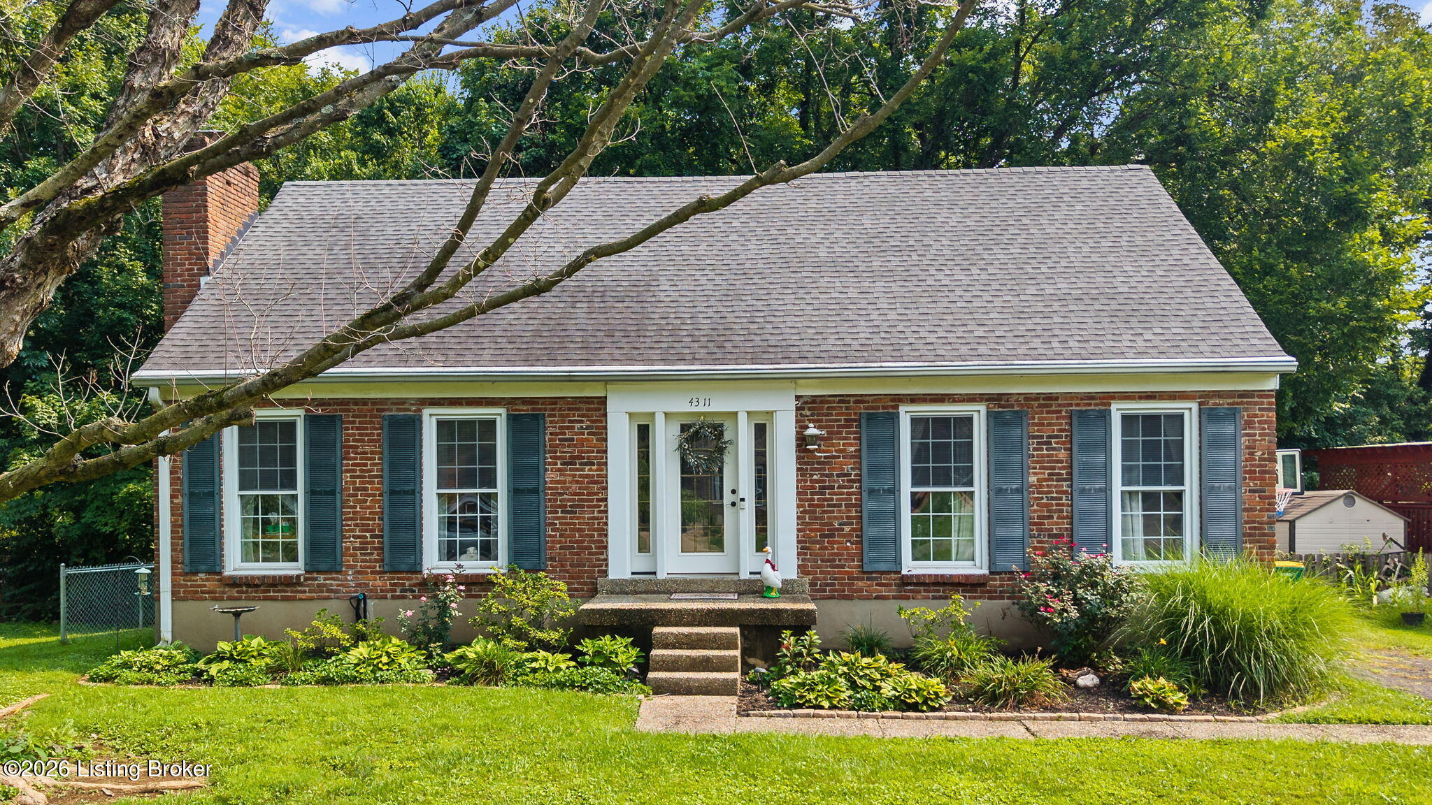 Red-brick home with dark shutters, a broad gray roof, and landscaped front yard.