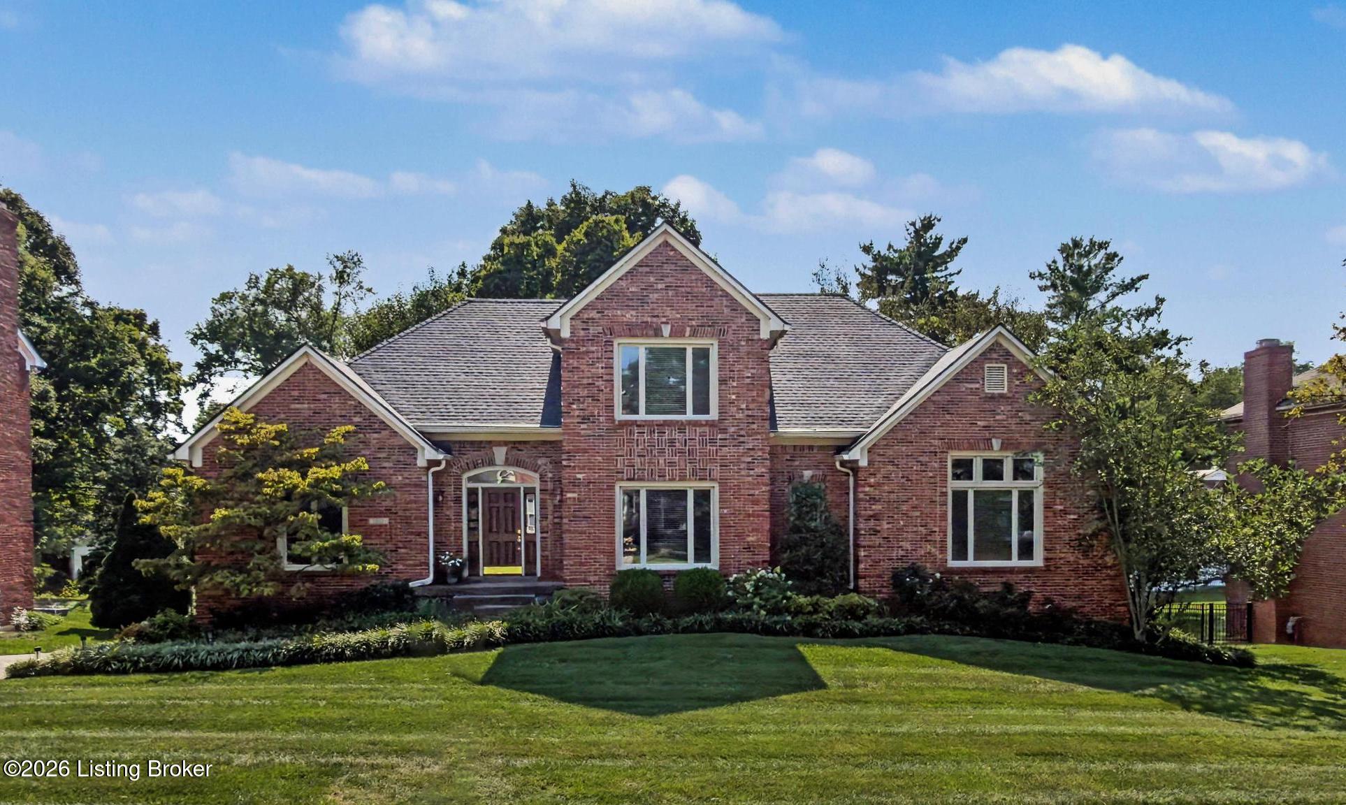 Red-brick house with multiple gables, white-trimmed windows, landscaped shrubs, and a broad front lawn.