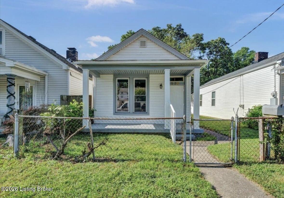 Small white house with a covered front porch, chain-link fence, and narrow walkway.