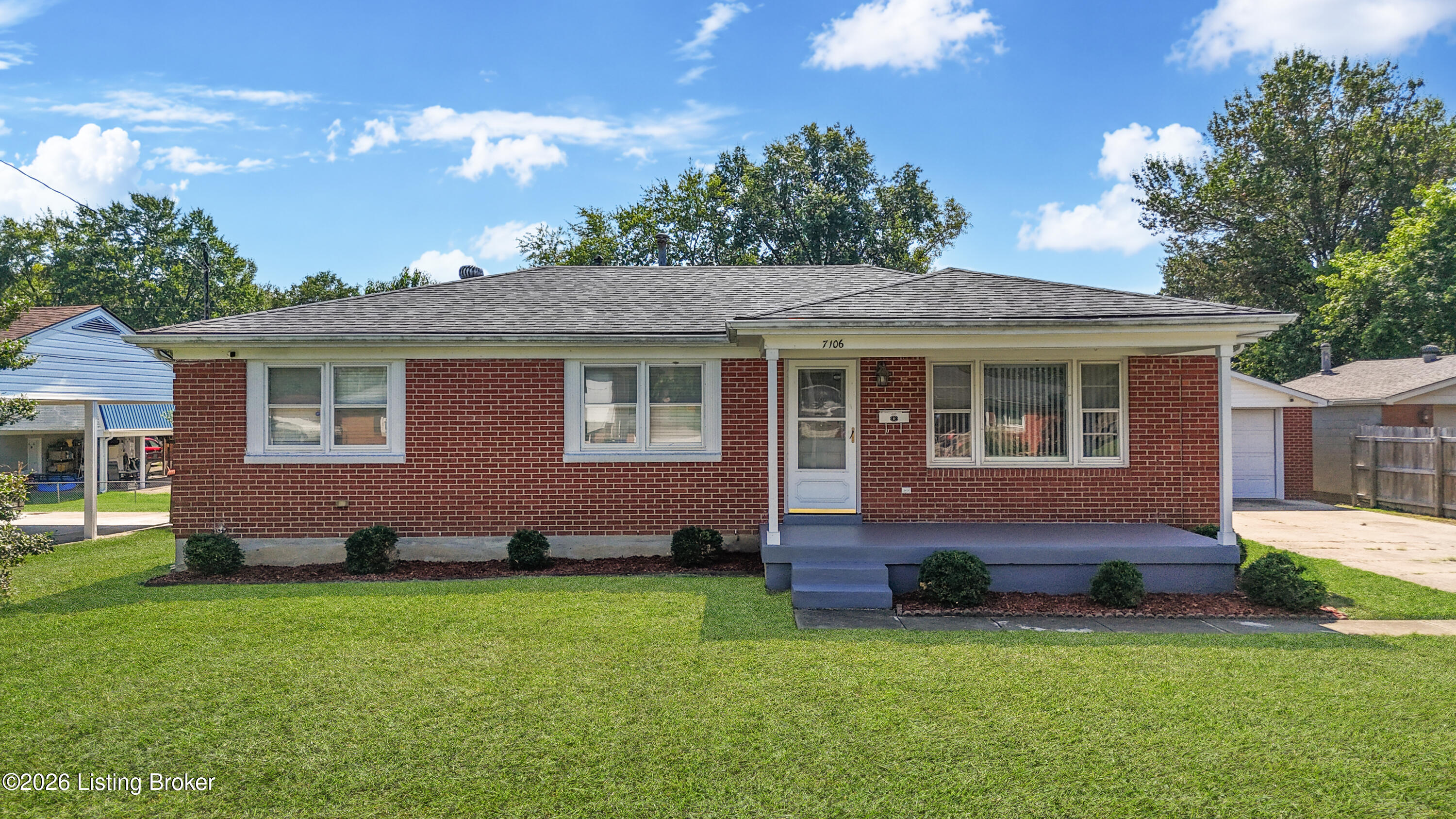 Red-brick ranch home with a covered front porch and broad green lawn.