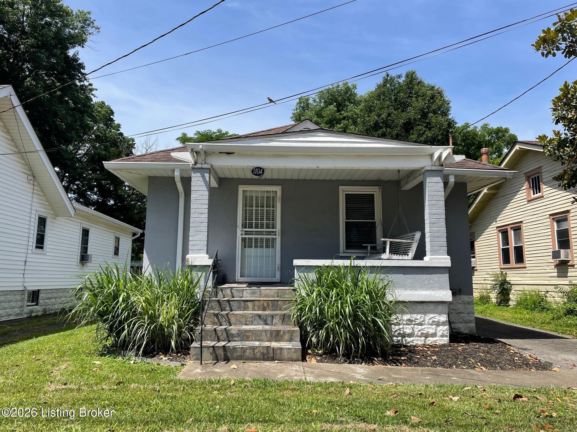 Gray house with a covered porch, white brick columns, stone steps, and a hanging swing.