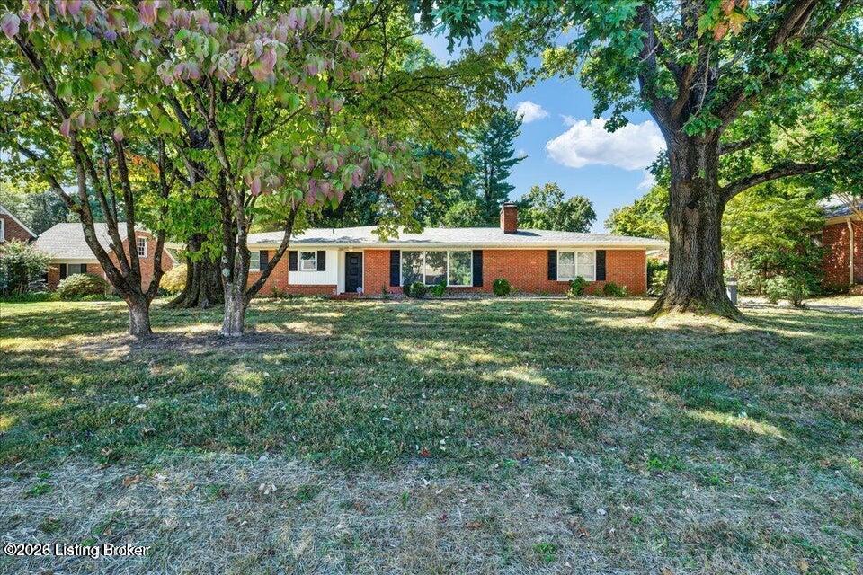 Single-story brick ranch house framed by mature trees, with a broad front lawn.