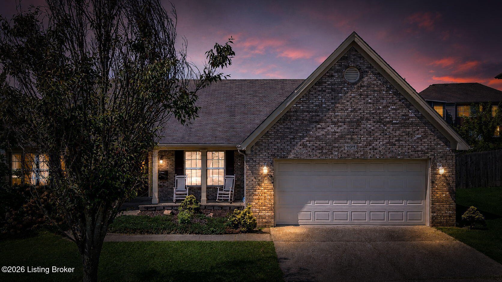 Brick home with a gabled roof, two-car garage, and warmly lit porch at dusk.