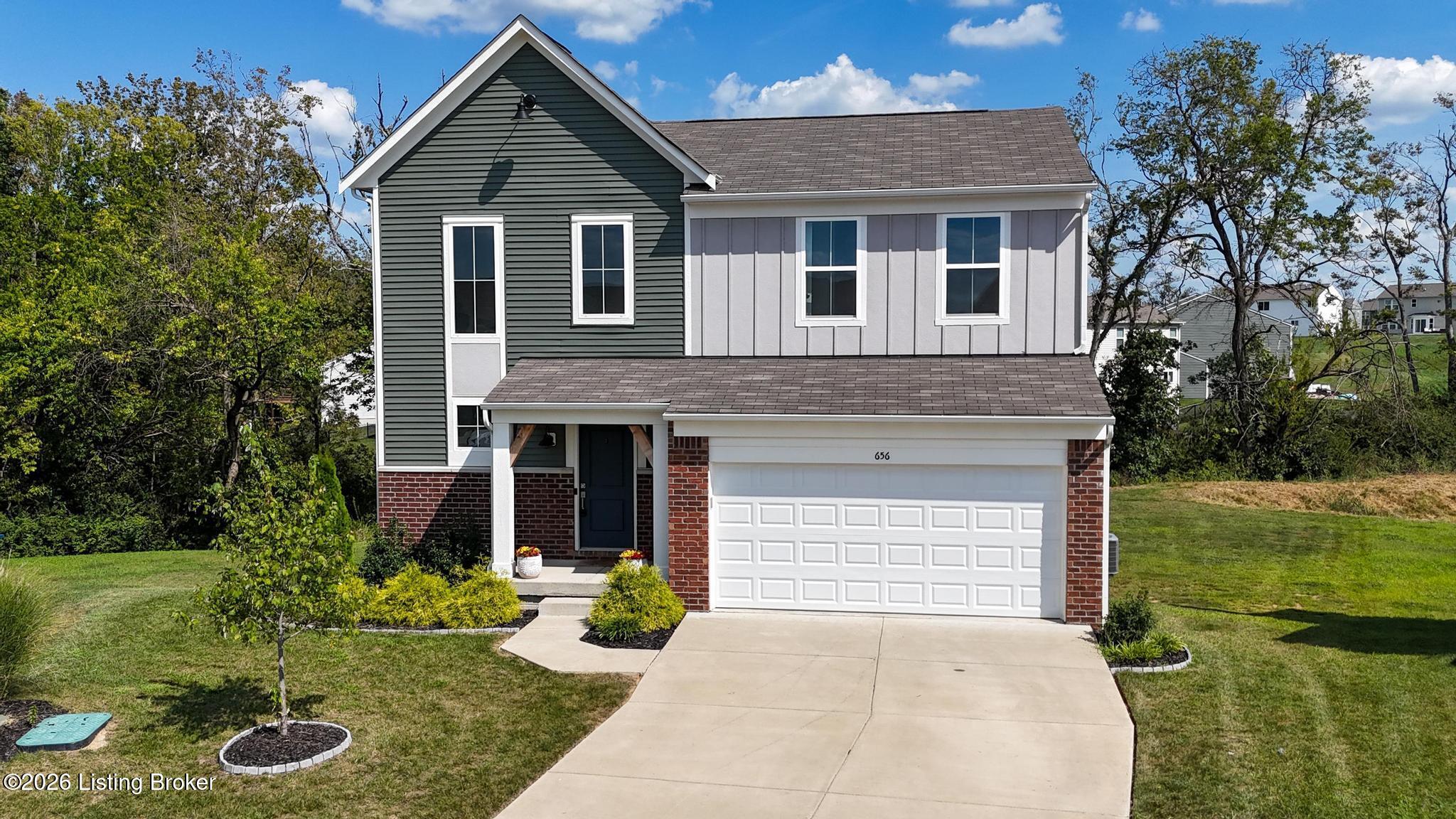 Two-story house with gray siding, brick accents, white double garage door, and curved driveway.